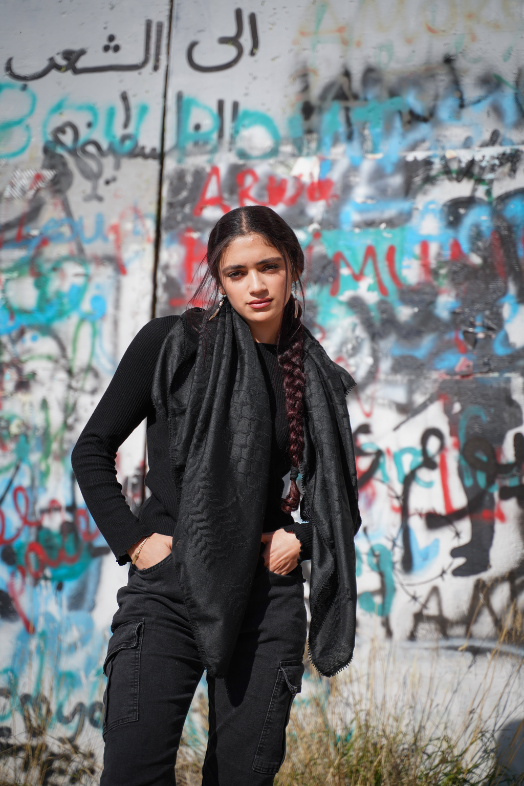 Unsere Black Edition Kufiya in schwarz getragen vor der Grenzmauer in Palästina