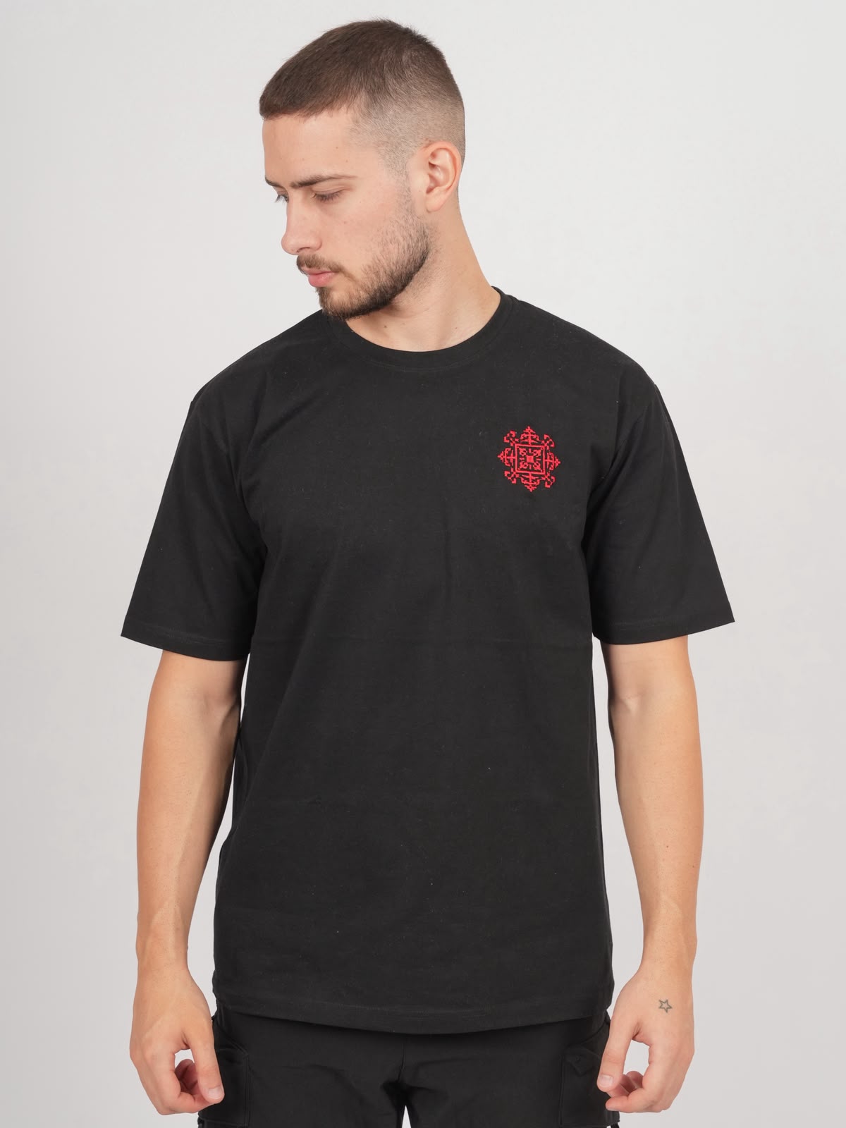 Männliches Model trägt schwarzes Jerusalem Tatreez T-Shirt mit roter Stickerei auf der linken Brust