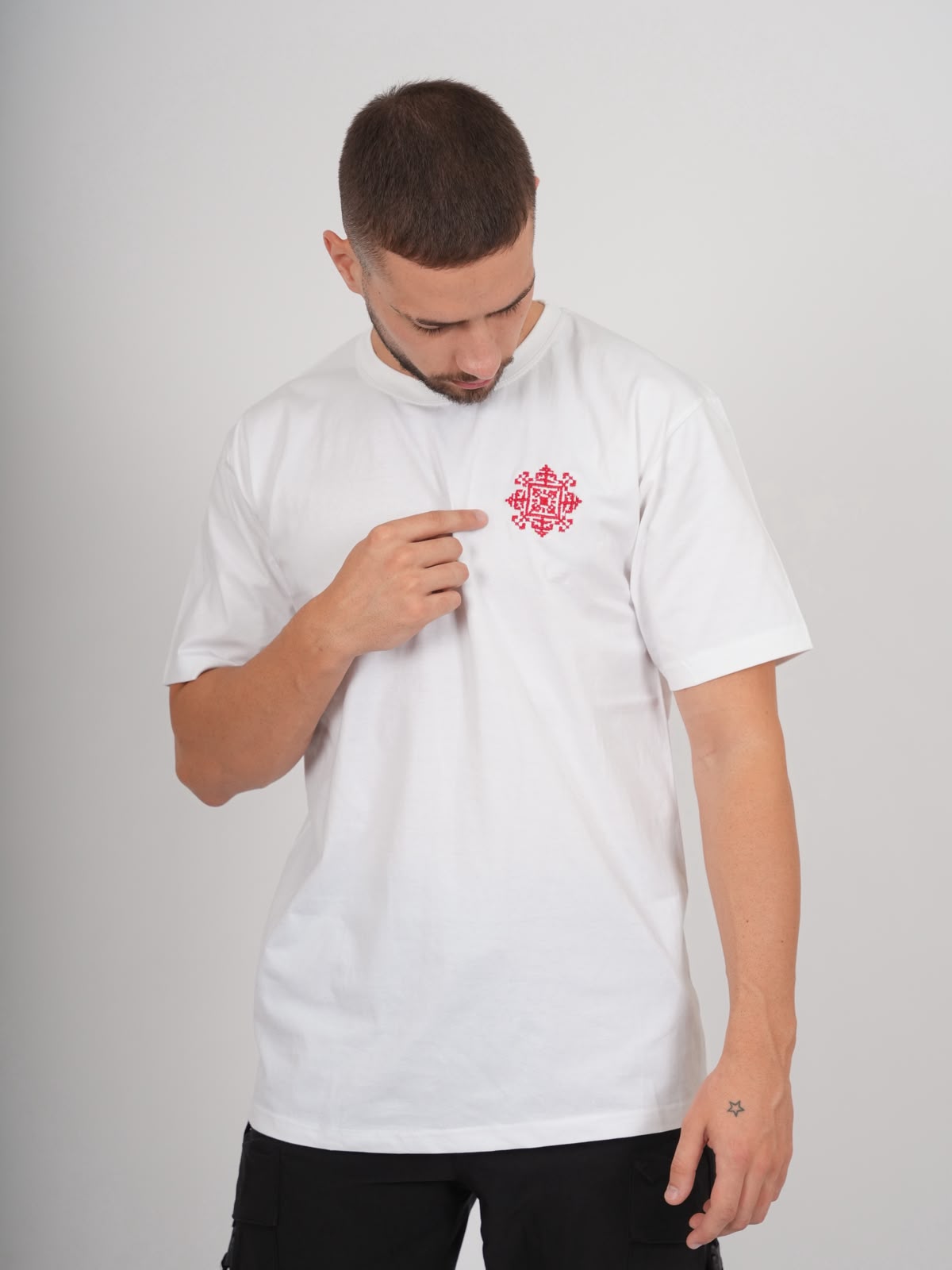 Männliches Model trägt weißes Jerusalem Tatreez T-Shirt mit roter Stickerei auf der linken Brust